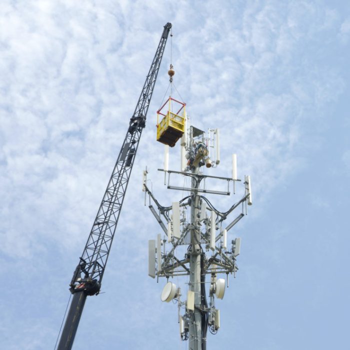 A Cellular/Television/Radio/Communications Tower is being constructed with the aid of a large crane.